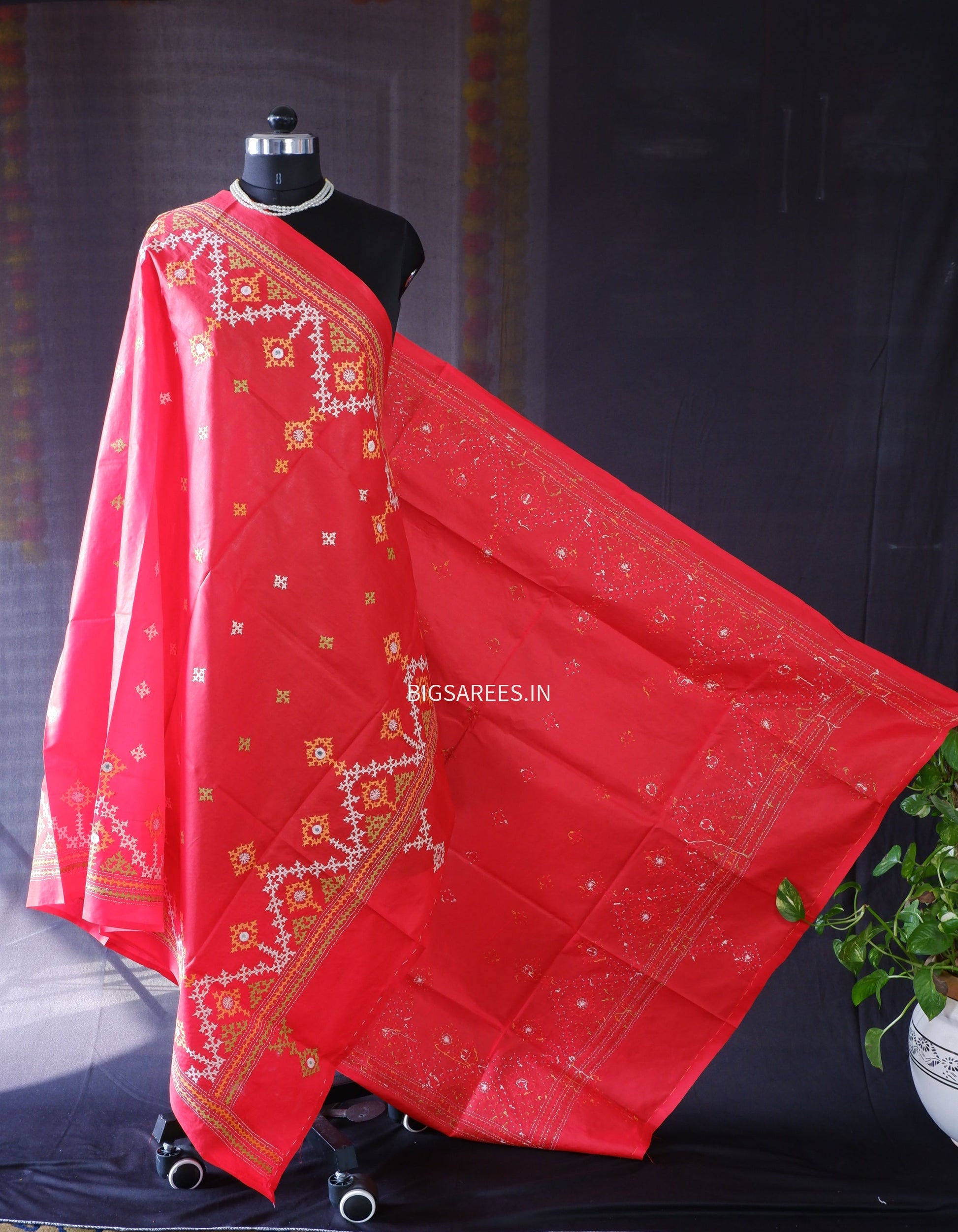 Red saree with gold patterns on a mannequin against a black background